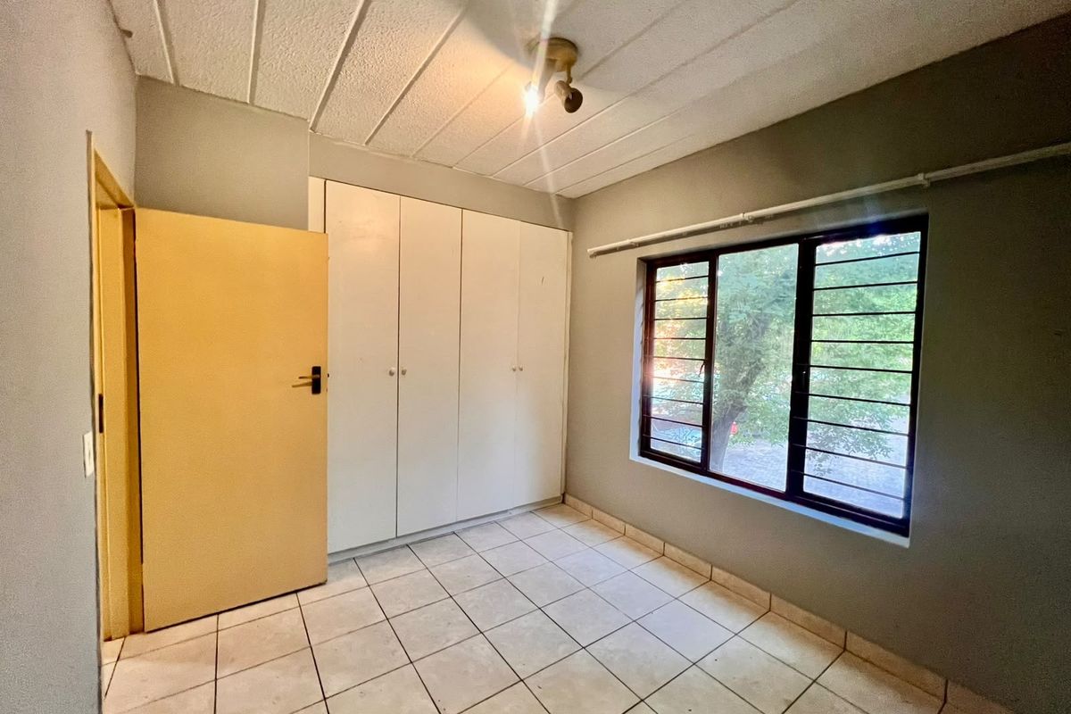 An empty bedroom featuring tiled flooring, built-in cupboards, and a window with security bars, offering a blank canvas for renovation.
