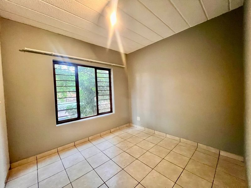 An empty bedroom featuring neutral wall paint, tiled flooring, and a window fitted with security bars.