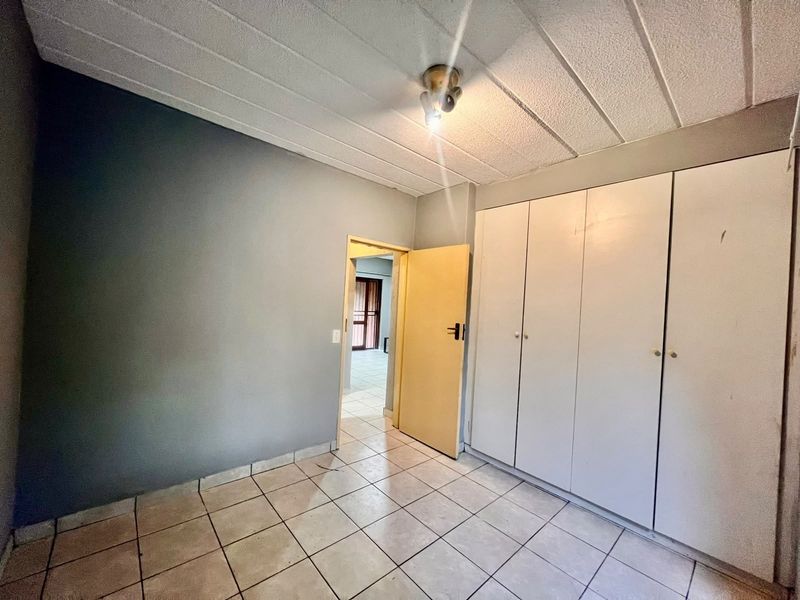 An empty bedroom featuring tiled flooring, built-in cupboards, and a textured ceiling, offering a blank canvas for renovation or interior design updates.