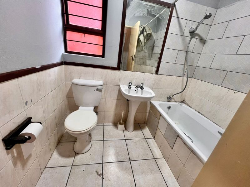 A dated bathroom featuring a pedestal basin, toilet, and bathtub with a handheld shower attachment, requiring cosmetic updates and maintenance to the tiling and sealant.