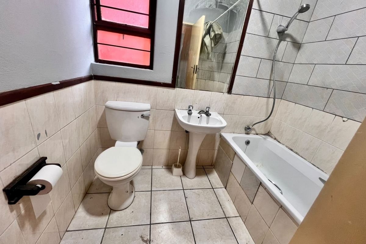 A dated bathroom featuring a pedestal basin, toilet, and bathtub with a handheld shower attachment, requiring cosmetic updates and maintenance to the tiling and sealant.