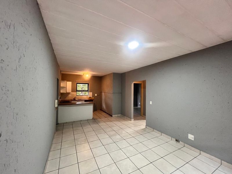 An open-plan living and kitchen area featuring tiled flooring, textured grey walls, and basic kitchen cabinetry in a vacant apartment setting.