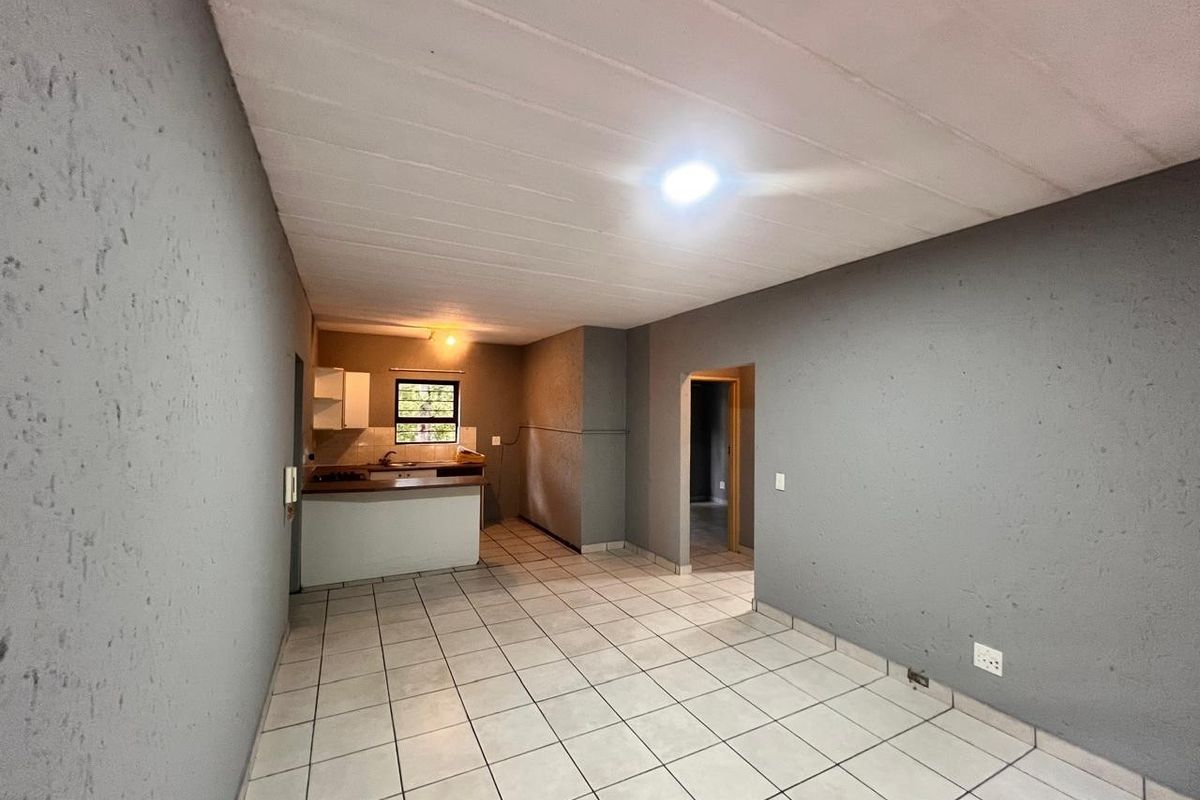 An open-plan living and kitchen area featuring tiled flooring, textured grey walls, and basic kitchen cabinetry in a vacant apartment setting.