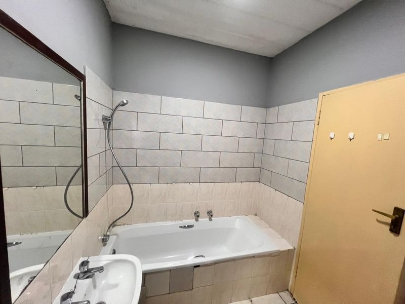 A functional bathroom featuring a built-in bathtub with shower attachment, pedestal basin, and tiled wall finishes, ready for cosmetic updates.