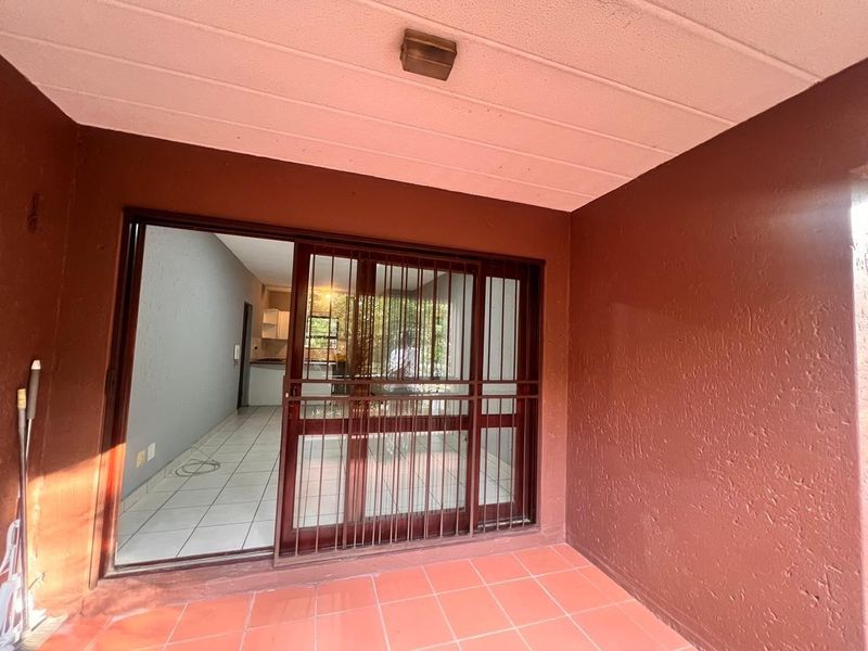 A covered patio area featuring tiled flooring and a sliding glass door with security gate, providing access to the interior living space.