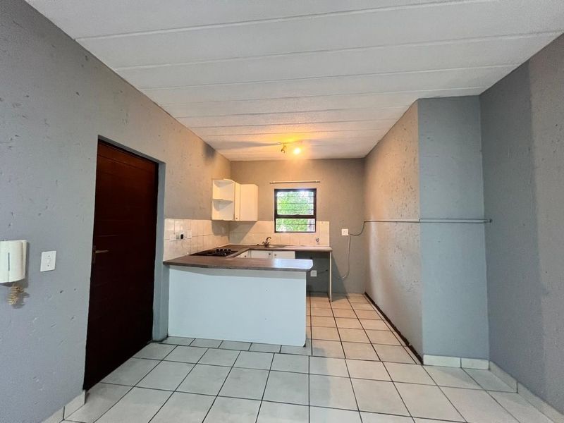 A compact, empty kitchen featuring tiled flooring, built-in cabinetry with a gas hob, and a tiled backsplash, ready for modernization.