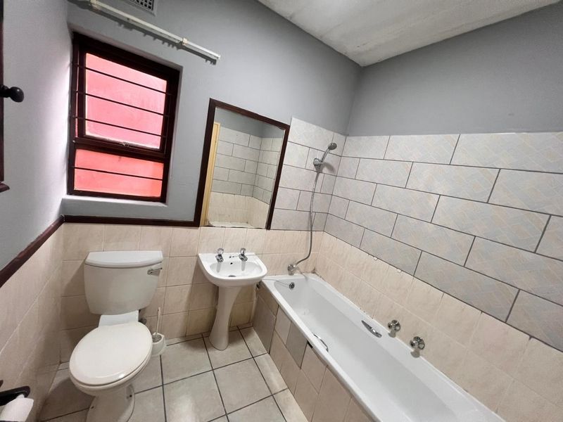 A functional bathroom featuring a pedestal basin, bathtub with handheld shower, and tiled finishes. The space is ready for cosmetic updates and modernization.