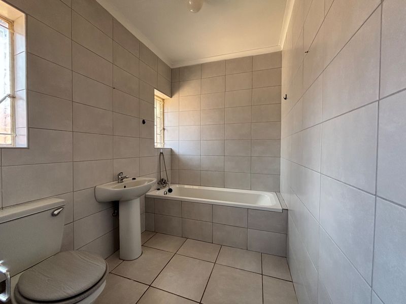 A functional bathroom featuring neutral ceramic wall and floor tiles, a pedestal basin, and a built-in bathtub with shower mixer.