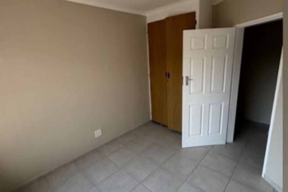 An empty bedroom featuring neutral wall paint, tiled flooring, and built-in wooden cupboards.