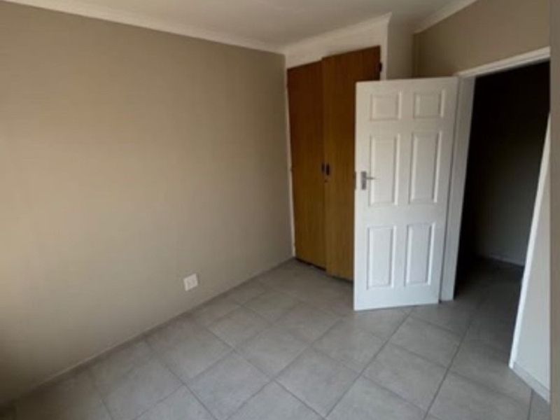 An empty bedroom featuring neutral wall paint, tiled flooring, and built-in wooden cupboards.