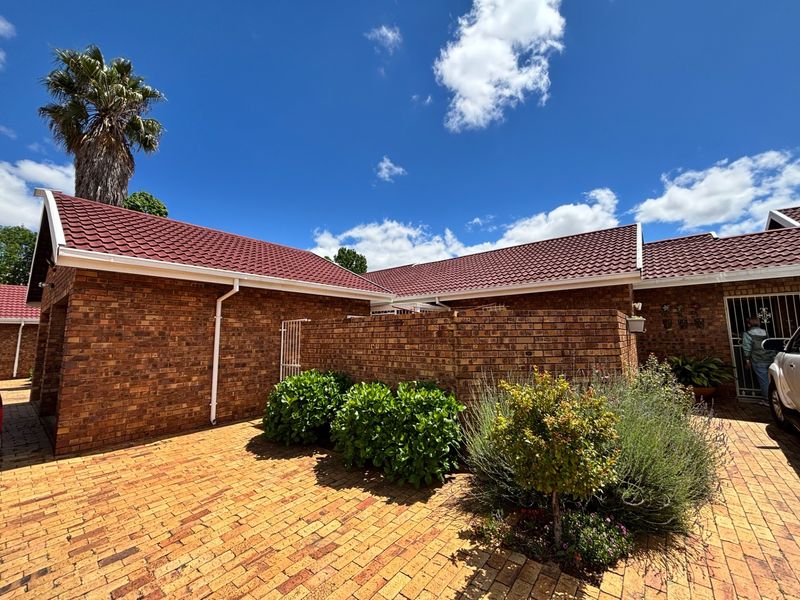 A well-maintained townhouse exterior featuring classic face brick construction, a tiled roof, and a paved driveway entrance.