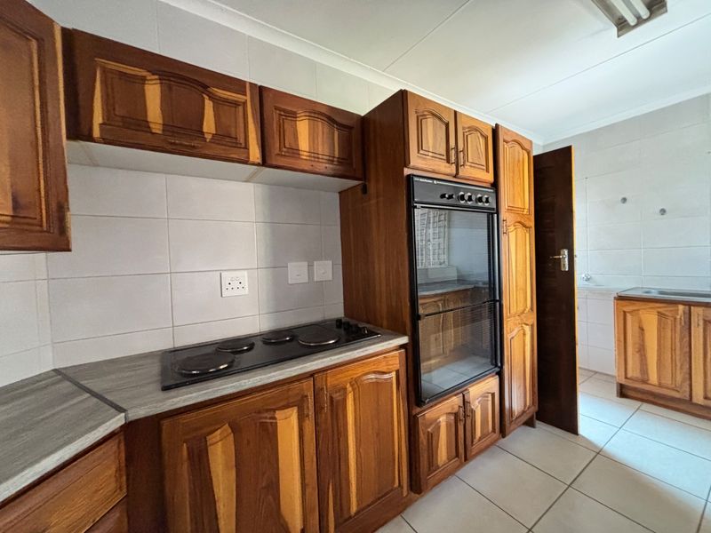 A functional kitchen featuring traditional wooden cabinetry, a built-in oven, electric hob, and tiled splashbacks, offering a classic layout ready for modernization.