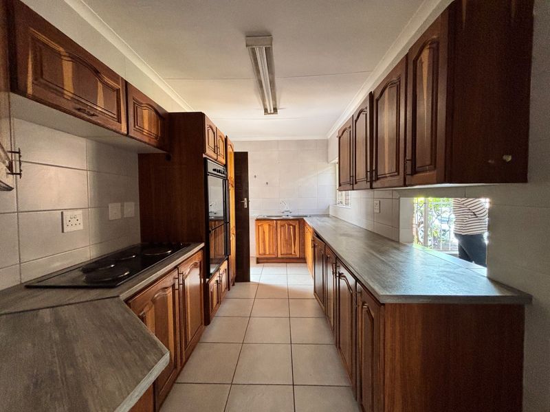 A functional galley-style kitchen featuring traditional wooden cabinetry, laminate countertops, built-in oven, electric hob, and tiled flooring throughout.