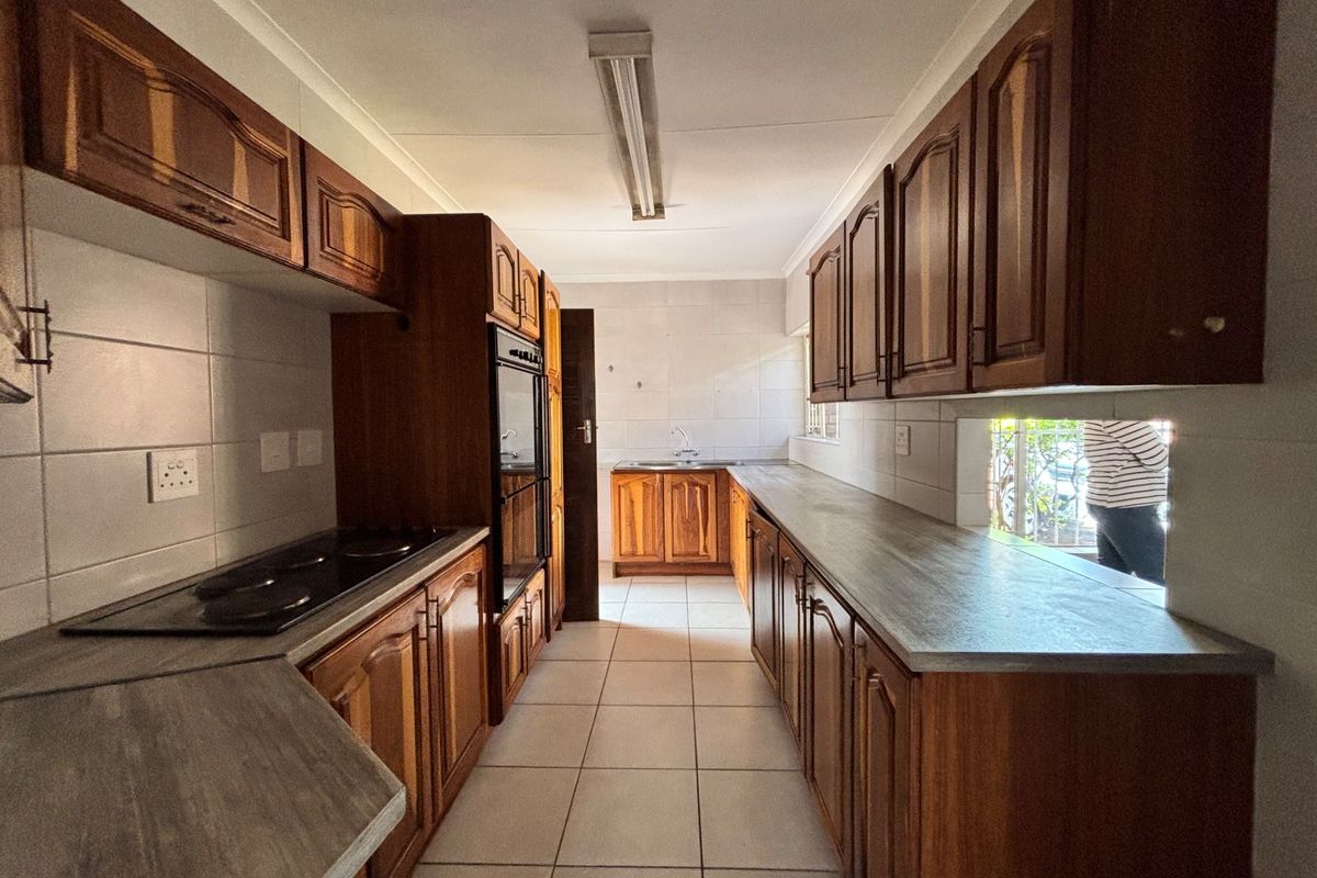 A functional galley-style kitchen featuring traditional wooden cabinetry, laminate countertops, built-in oven, electric hob, and tiled flooring throughout.