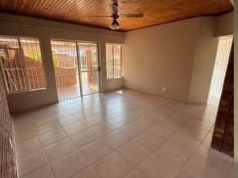 An empty living area featuring tiled flooring, a timber-clad ceiling with a ceiling fan, and sliding glass doors leading to the exterior.