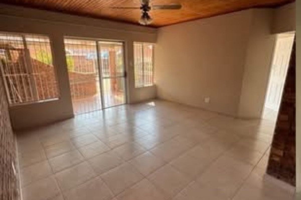 An empty living area featuring tiled flooring, a timber-clad ceiling with a ceiling fan, and sliding glass doors leading to the exterior.