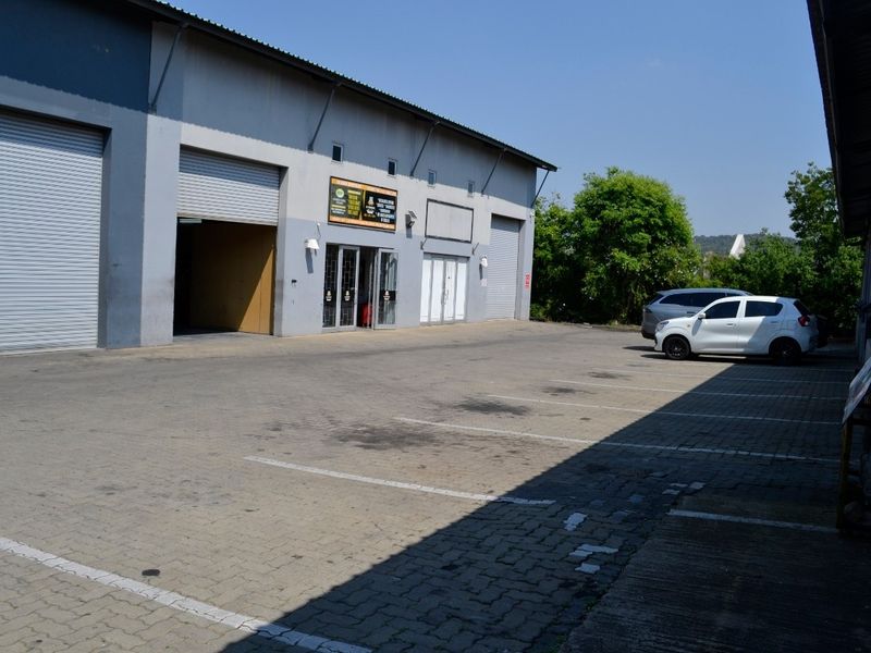 Industrial warehouse exterior featuring multiple roller shutter doors, paved parking area, and metal cladding facade.