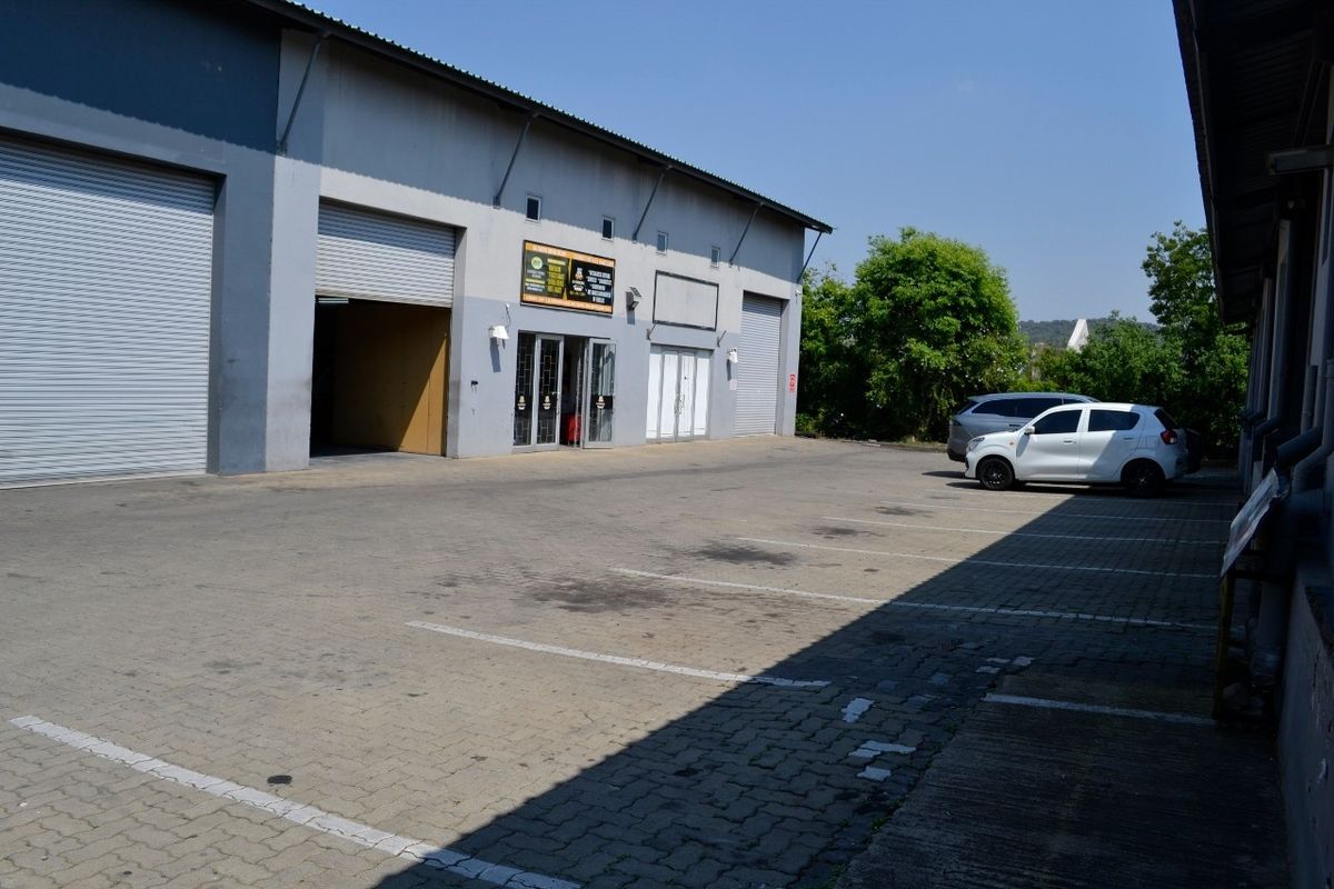Industrial warehouse exterior featuring multiple roller shutter doors, paved parking area, and metal cladding facade.