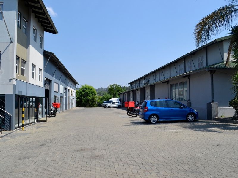 Exterior view of an industrial complex featuring paved driveway access, multiple warehouse units with roller shutter doors, and modern multi-story office facade.