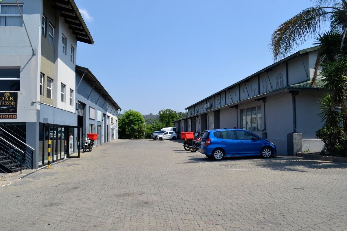 Exterior view of an industrial complex featuring paved driveway access, multiple warehouse units with roller shutter doors, and modern multi-story office facade.