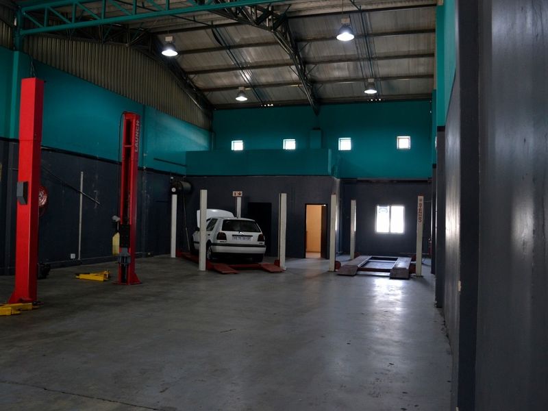 Spacious industrial workshop featuring concrete flooring, exposed steel roof trusses, and multiple built-in vehicle lifts for automotive maintenance operations.