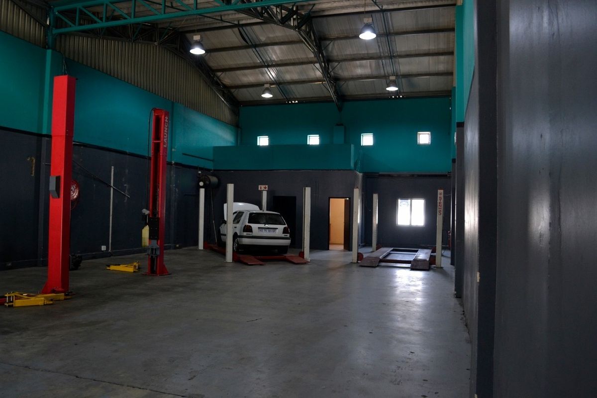 Spacious industrial workshop featuring concrete flooring, exposed steel roof trusses, and multiple built-in vehicle lifts for automotive maintenance operations.