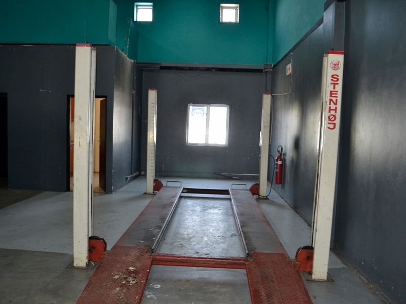 Industrial garage space featuring a fixed two-post vehicle lift, concrete flooring, and high-level windows, suitable for automotive maintenance or workshop use.