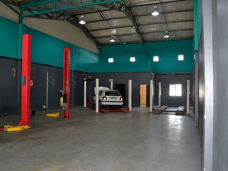 Spacious industrial workshop featuring high ceilings with exposed steel trusses, concrete flooring, and multiple professional-grade vehicle lifts for automotive maintenance.