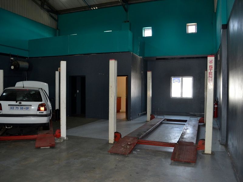 Industrial workshop space featuring a two-post vehicle lift, high ceilings, mezzanine level, and concrete flooring, suitable for automotive or light industrial operations.