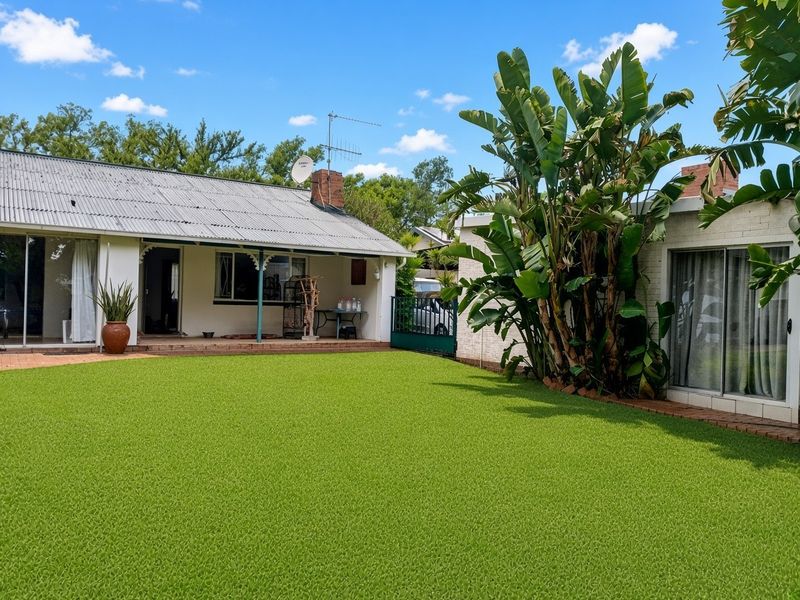 Rear view of the property featuring a covered patio, artificial lawn, and established garden greenery.