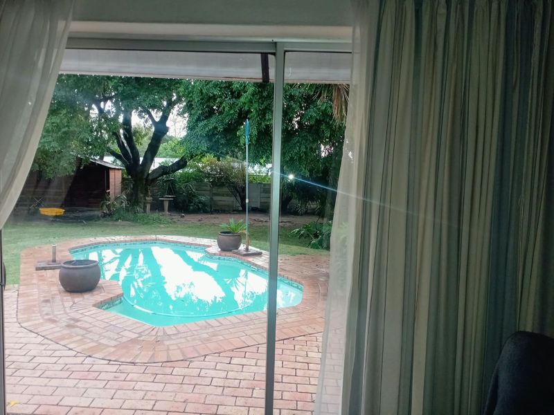 View from an interior room looking out onto a backyard swimming pool with brick paving and established garden surroundings.