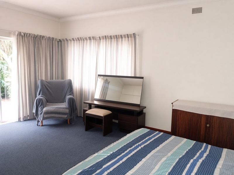 A spacious bedroom featuring blue carpeting, neutral walls, and a sliding glass door providing access to the exterior.