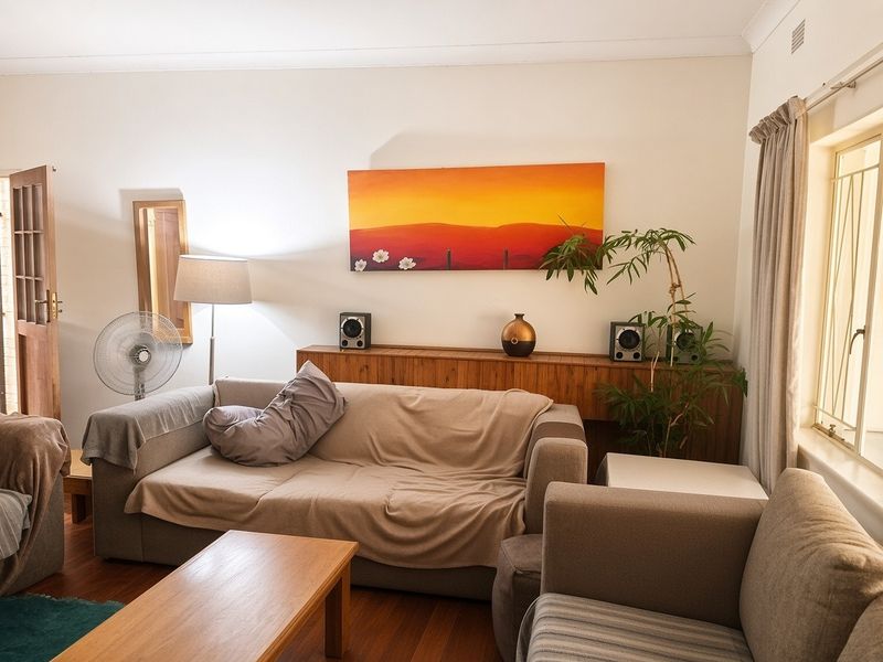 A comfortable living room featuring timber flooring and natural light through a window fitted with security bars.