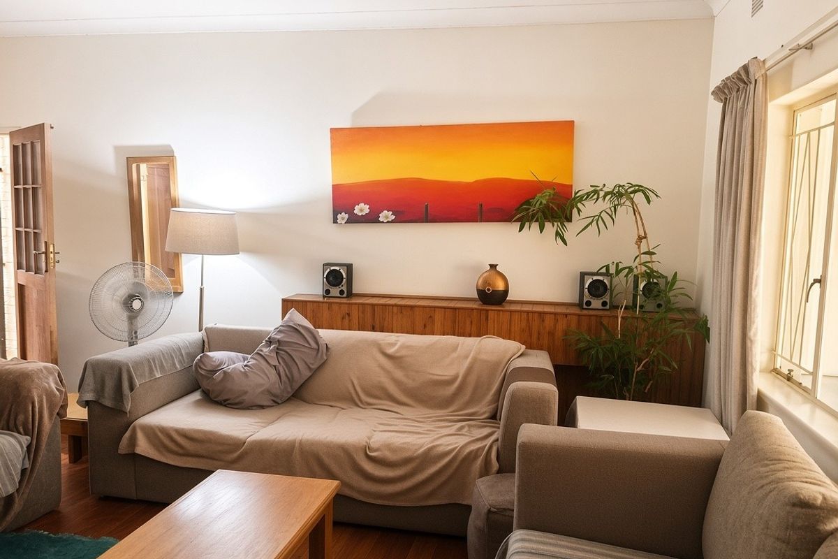 A comfortable living room featuring timber flooring and natural light through a window fitted with security bars.
