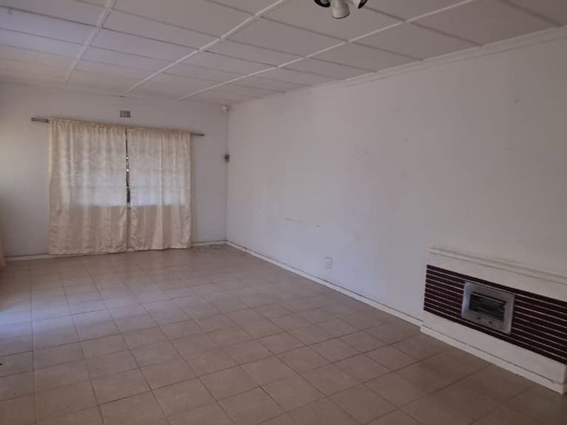 Spacious living area featuring tiled flooring, a built-in gas heater, and a suspended ceiling, offering a blank canvas for renovation.