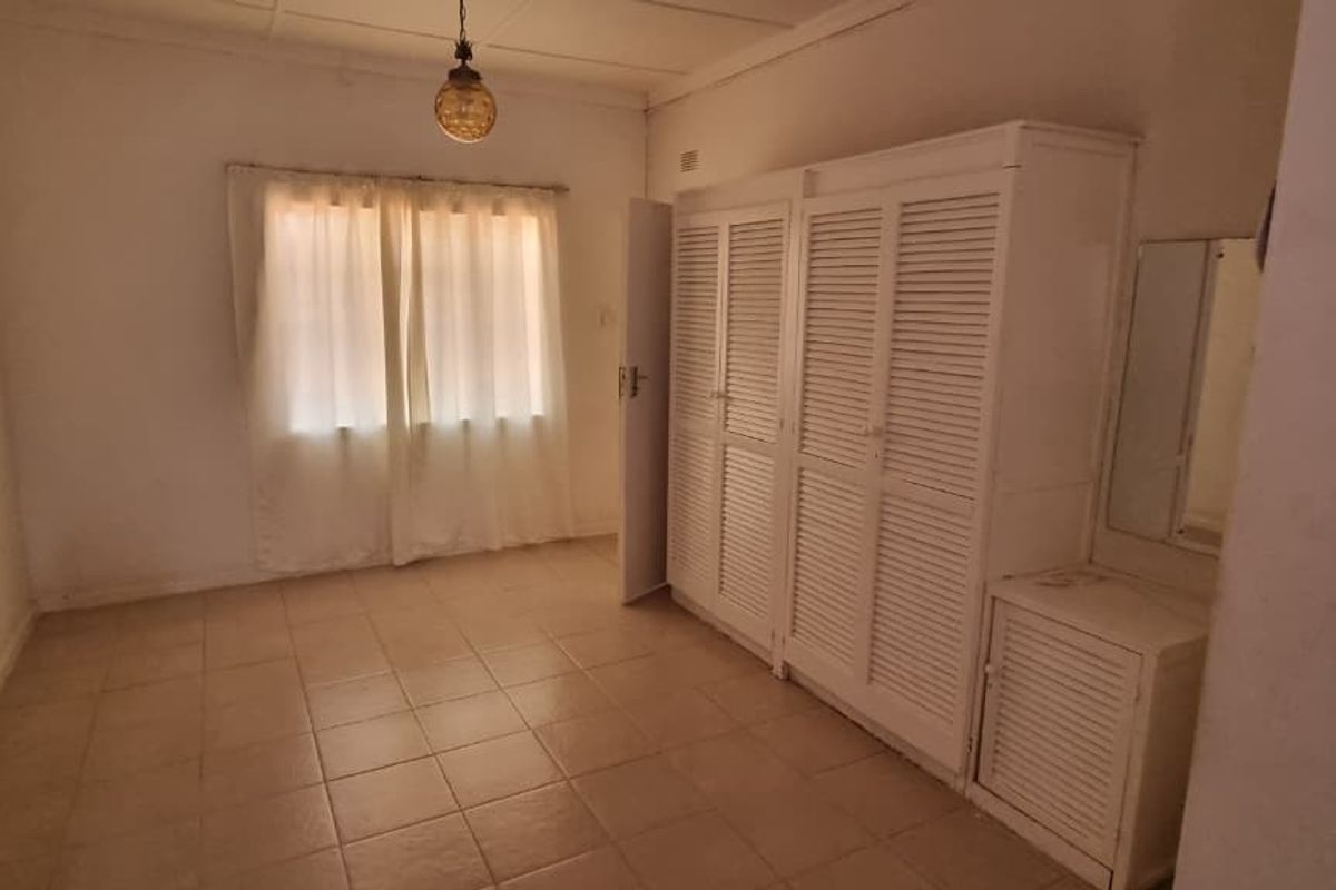 A bedroom featuring built-in white louvered cupboards and tiled flooring, offering a functional space ready for modernization and updated interior styling.