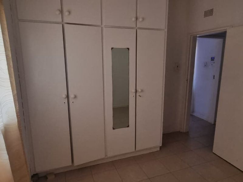 A bedroom featuring built-in cupboards with a central mirror and tiled flooring, offering a functional space ready for personalization.