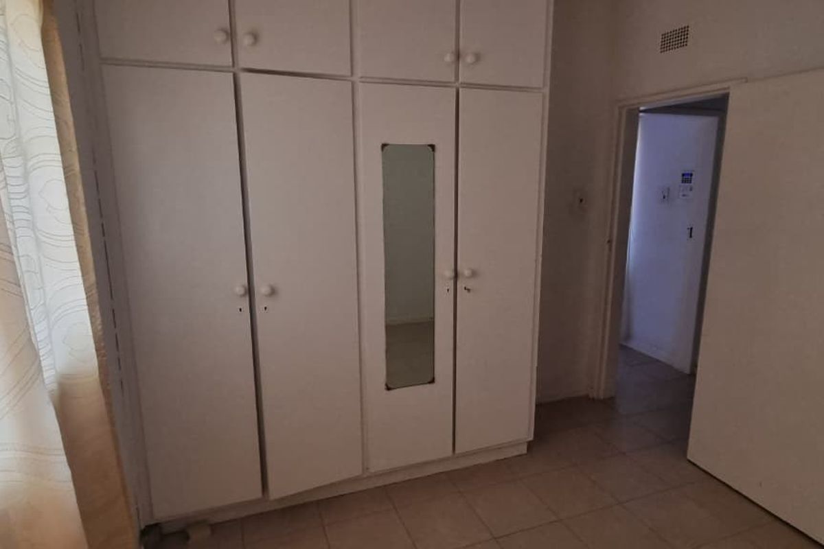 A bedroom featuring built-in cupboards with a central mirror and tiled flooring, offering a functional space ready for personalization.