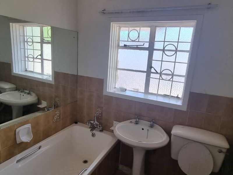 A functional bathroom featuring a pedestal basin, bathtub, and toilet with dated wall tiling and security bars on the window.
