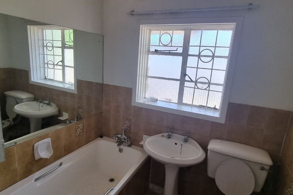 A functional bathroom featuring a pedestal basin, bathtub, and toilet with dated wall tiling and security bars on the window.
