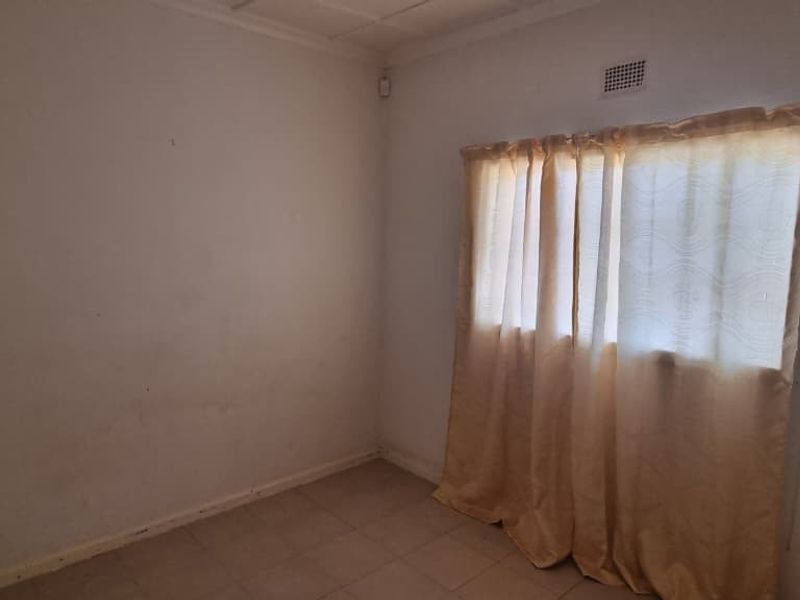 An empty bedroom featuring tiled flooring and a ceiling vent, requiring cosmetic updates to the wall finishes.