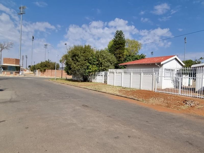 Street view showing the property frontage, perimeter fencing, and surrounding neighbourhood infrastructure with nearby floodlight masts.