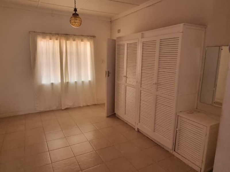 A bedroom featuring built-in white louvered cupboards and tiled flooring, offering a functional space ready for modernization and updated interior styling.