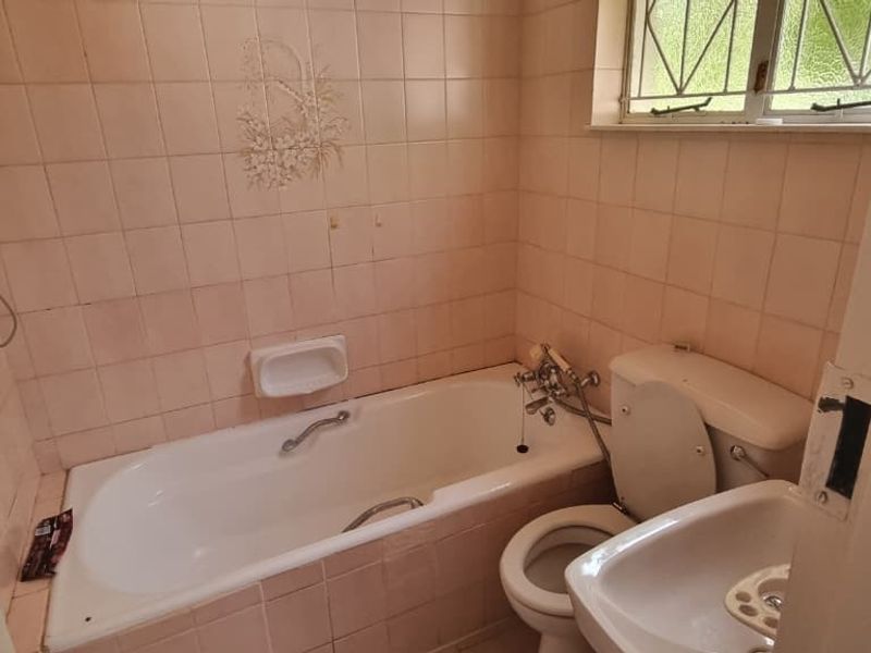 A dated bathroom featuring a standard bathtub, toilet, and pedestal basin with original wall tiling, offering potential for a modern renovation.