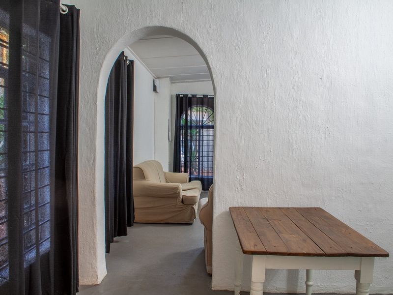 A living area featuring a distinctive arched doorway, textured white walls, and concrete flooring, offering a rustic foundation for potential interior updates.