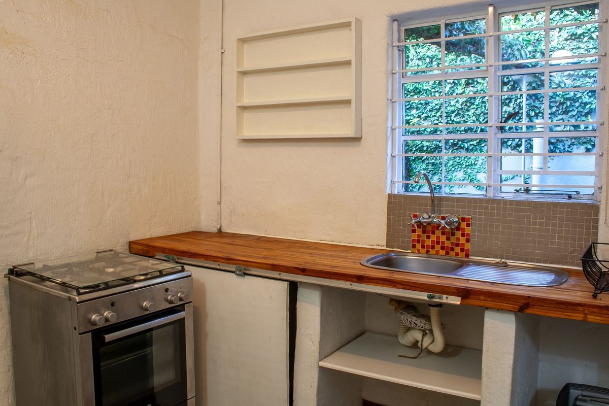 A compact kitchen area featuring a wooden countertop, stainless steel sink, and a freestanding gas stove with security bars on the window.
