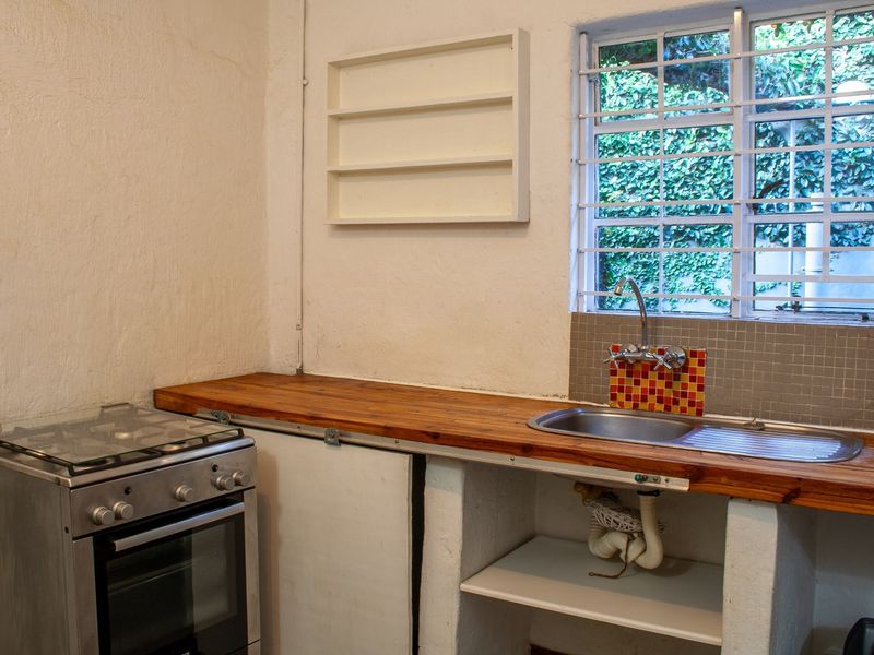 A compact kitchen area featuring a wooden countertop, stainless steel sink, and a freestanding gas stove with security bars on the window.