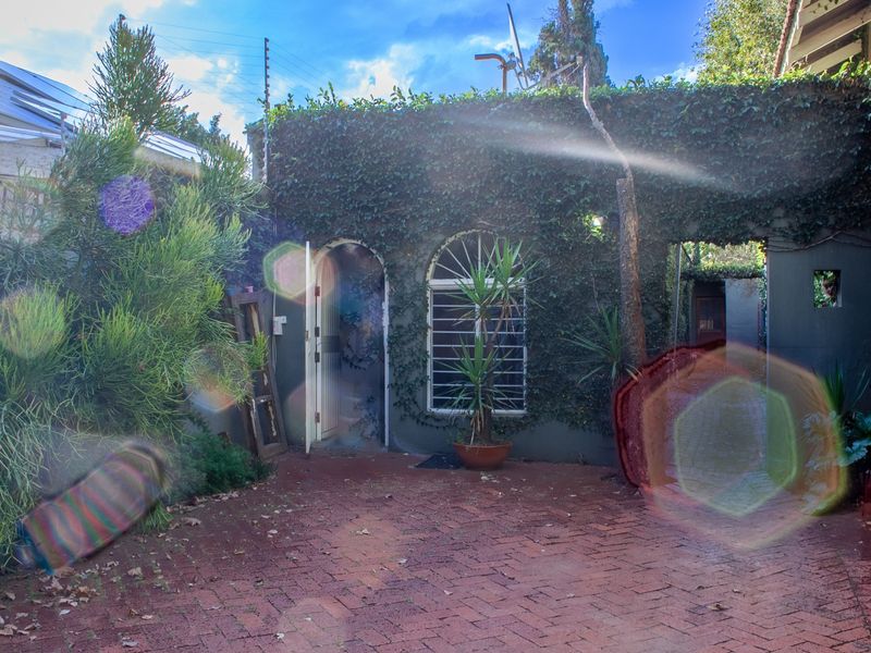 A rear courtyard area featuring brick paving, an arched entrance, and walls covered in climbing ivy, secured with electric fencing.