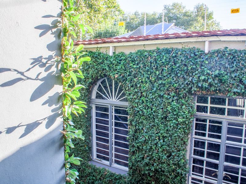 A view of the rear exterior wall featuring climbing ivy, arched windows with security bars, and terracotta roof tiles.