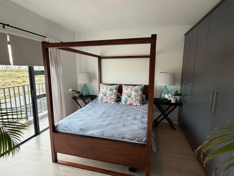 A well-maintained bedroom featuring modern built-in cupboards, laminate flooring, and a large sliding glass door providing access to a balcony.